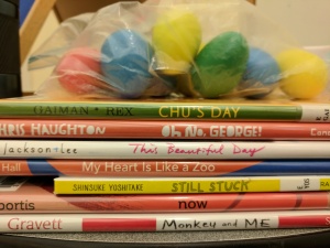 Stack of picture books with bag of shaker eggs on top