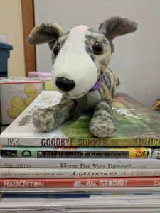 Greyhound stuffed animal on stack of picture books